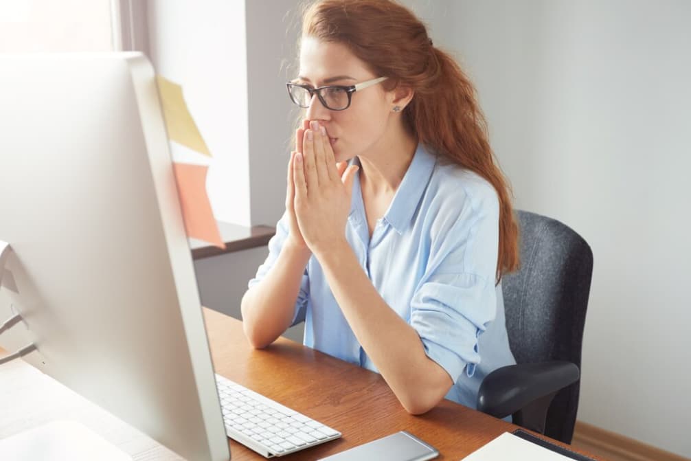 A concerned woman with glasses is staring intently at a computer screen